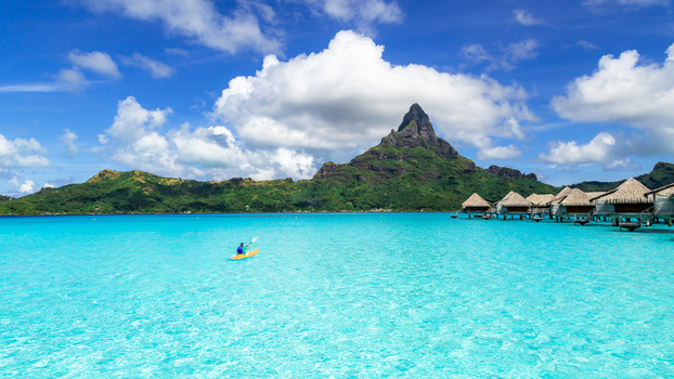 View of a person kayaking in the turquoise lagoon of Bora Bora with Mount Otemanu in the background and overwater bungalows Bora Bora Leeward Islands French Polynesia.