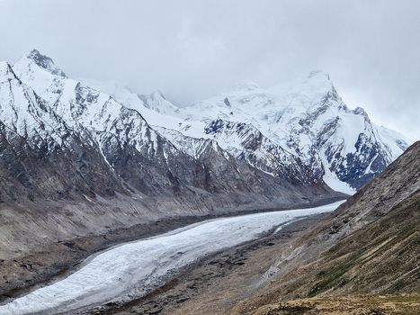 View of Drang Drung Glacier a massive river of ice surrounded by rugged snow capped Himalayan peaks under a cloudy sky in Zanskar Ladakh India.
