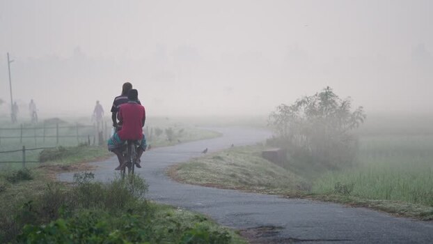 View of people cycling on a foggy rural road in Bogura Bangladesh.