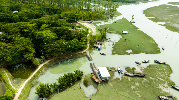 Aerial view of small wooden boats moored in the shallow waters of a riverine landscape surrounded by lush green trees and vegetation in Patharghata Barisal Division Bangladesh. Aerial view of small wooden boats moored in the shallow waters of a riverine landscape surrounded by lush green trees and vegetation in Patharghata Barisal Division Bangladesh.