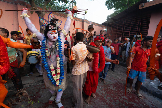 Munshiganj Bangladesh 13 April 2025 View of blue painted Shiva devotee with trishul leads a vibrant procession of orange clad figures on a dusty street. Munshiganj Bangladesh 13 April 2025 View of blue painted Shiva devotee with trishul leads a vibrant procession of orange clad figures on a dusty street.