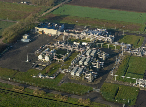 Aerial view of the natural gas mining facility featuring industrial pipelines storage tanks and technical buildings surrounded by green agricultural fields in Slochteren Groningen Netherlands. Aerial view of the natural gas mining facility featuring industrial pipelines storage tanks and technical buildings surrounded by green agricultural fields in Slochteren Groningen Netherlands.