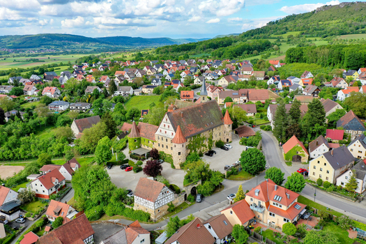 Aerial view of Schloss Wiesenthau surrounded by traditional red roofed houses and lush green hills under a bright sky in Wiesenthau Bayern Germany. Aerial view of Schloss Wiesenthau surrounded by traditional red roofed houses and lush green hills under a bright sky in Wiesenthau Bayern Germany.