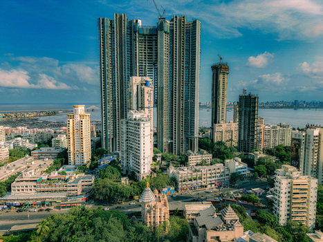 Aerial view of modern skyscrapers under construction and a traditional temple surrounded by lush green trees near the coastline Mumbai Maharashtra India. Aerial view of modern skyscrapers under construction and a traditional temple surrounded by lush green trees near the coastline Mumbai Maharashtra India.