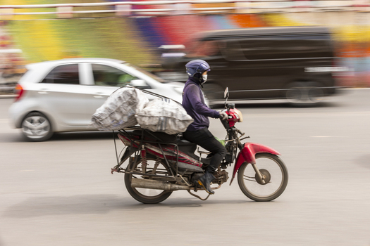 Hanoi Vietnam 11 November 2025 View of a motorcyclist carrying large heavy bags on a red motorbike navigating through busy city traffic with motion blur.