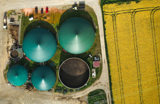 Aerial view of a biogas plant with green storage tanks and farm machinery next to a yellow rapeseed field in Hofgeismar Hessen Germany. Aerial view of a biogas plant with green storage tanks and farm machinery next to a yellow rapeseed field in Hofgeismar Hessen Germany.
