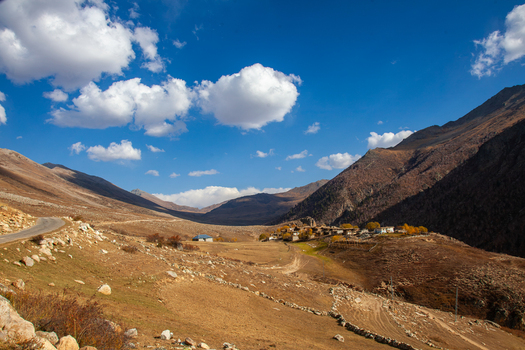 View of Deosai National Park with a small mountain village winding dirt road and autumn colored trees under a bright blue sky in Astore Gilgit Pakistan. View of Deosai National Park with a small mountain village winding dirt road and autumn colored trees under a bright blue sky in Astore Gilgit Pakistan.