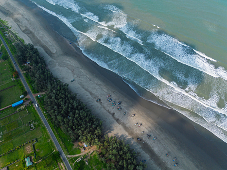 Aerial view of the sandy shoreline of Cox s Bazar beach with rolling waves fishing boats and a green tree line bordering a coastal road in Cox s Bazar Chittagong Division Bangladesh. Aerial view of the sandy shoreline of Cox s Bazar beach with rolling waves fishing boats and a green tree line bordering a coastal road in Cox s Bazar Chittagong Division Bangladesh.
