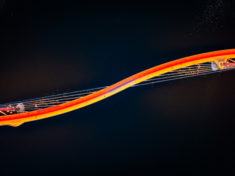 Aerial view of the illuminated Boorloo Bridge at night showcasing its distinctive curved design and cable stayed structure over the dark water in East Perth Western Australia Australia.
