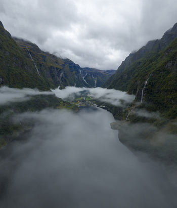 Aerial view of Sognefjord with steep mountains cascading waterfalls and low clouds drifting over the dark water near Gudvangen Vestland Norway.