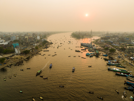 Aerial view of Sadarghat on the Buriganga River with numerous boats navigating the water at sunset surrounded by the dense urban landscape of Dhaka Dhaka Division Bangladesh. Aerial view of Sadarghat on the Buriganga River with numerous boats navigating the water at sunset surrounded by the dense urban landscape of Dhaka Dhaka Division Bangladesh.