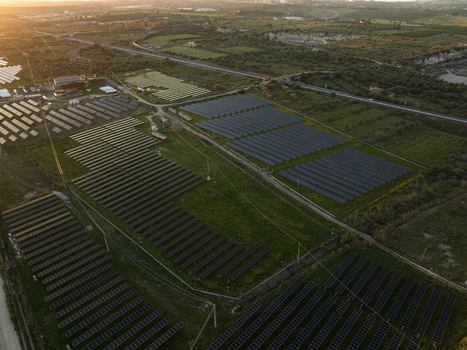 Aerial view of a large solar panel farm surrounded by green fields and rural roads under warm sunset light Augusta Sicily Italy. Aerial view of a large solar panel farm surrounded by green fields and rural roads under warm sunset light Augusta Sicily Italy.
