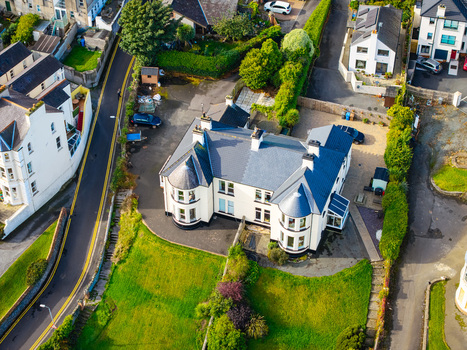 Aerial view of a residential building with a dark roof and white walls surrounded by green lawns and paved driveways in Bangor Northern Ireland United Kingdom.