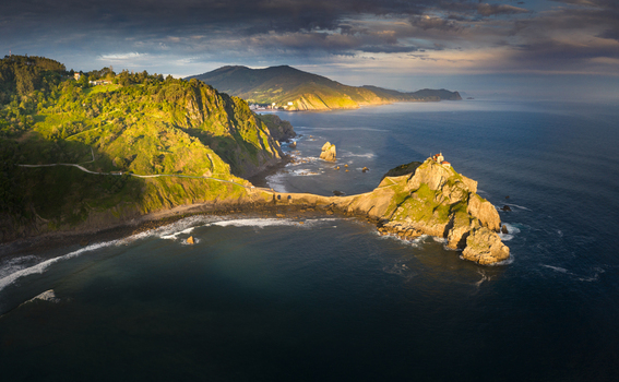 Aerial view of Gaztelugatxe islet and its hermitage connected by a stone bridge to the rugged coastline under a dramatic sunset sky Gaztelugatxeko Doniene Basque Country Spain. Aerial view of Gaztelugatxe islet and its hermitage connected by a stone bridge to the rugged coastline under a dramatic sunset sky Gaztelugatxeko Doniene Basque Country Spain.