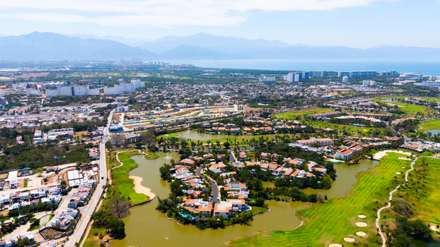 Aerial view of vibrant green golf courses meet the tranquil waters of island communities under a vast hazy sky Riviera Nayarit Mexico