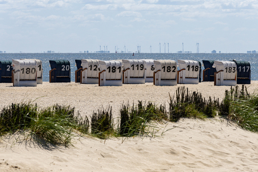 View of numbered traditional beach chairs on the sandy dunes of Strand Schillig under a bright sky in Wangerland Niedersachsen Germany. View of numbered traditional beach chairs on the sandy dunes of Strand Schillig under a bright sky in Wangerland Niedersachsen Germany.