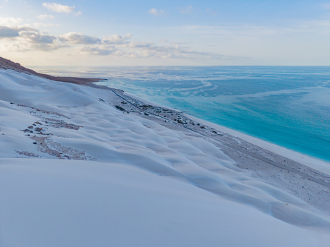 Aerial view of pure white sand dunes meet the turquoise sea under a pastel sky creating a surreal coastal landscape Erissel Socotra Yemen. Aerial view of pure white sand dunes meet the turquoise sea under a pastel sky creating a surreal coastal landscape Erissel Socotra Yemen.
