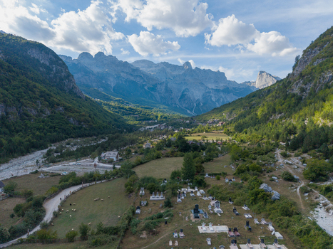 Aerial view of Theth village in the Albanian Alps featuring a cemetery scattered houses and a winding riverbed surrounded by lush green mountain slopes Theth Shkoder County Albania. Aerial view of Theth village in the Albanian Alps featuring a cemetery scattered houses and a winding riverbed surrounded by lush green mountain slopes Theth Shkoder County Albania.