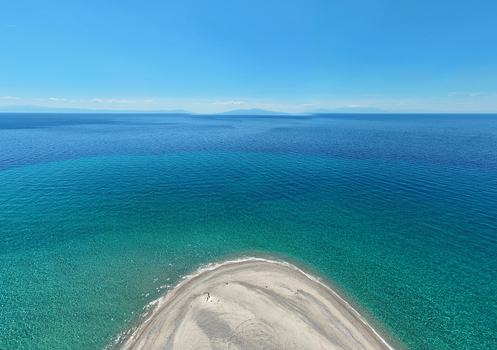 Aerial view of the sandy spit of Possidi Beach surrounded by the turquoise waters of the Aegean Sea under a clear blue sky Greece.