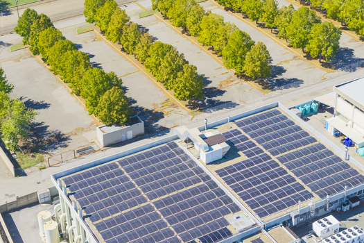 Aerial view of a commercial building featuring extensive rooftop solar panels adjacent to a parking lot lined with green trees in Arezzo Tuscany Italy. Aerial view of a commercial building featuring extensive rooftop solar panels adjacent to a parking lot lined with green trees in Arezzo Tuscany Italy.