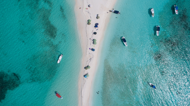 Aerial view of Los Roques archipelago featuring a narrow white sandbar surrounded by turquoise water with small boats anchored nearby in Los Roques Dependencias Federale Venezuela. Aerial view of Los Roques archipelago featuring a narrow white sandbar surrounded by turquoise water with small boats anchored nearby in Los Roques Dependencias Federale Venezuela.
