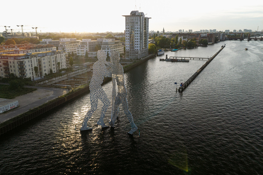 Aerial view of the Molecule Men sculpture standing in the Spree river with urban buildings and sunset light in the background in Berlin Berlin Germany. Aerial view of the Molecule Men sculpture standing in the Spree river with urban buildings and sunset light in the background in Berlin Berlin Germany.