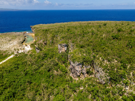 Aerial view of Chigit Beach with rugged limestone cliffs and lush tropical vegetation overlooking the deep blue Pacific Ocean in Northern Tinian Tinian Northern Mariana Islands. Aerial view of Chigit Beach with rugged limestone cliffs and lush tropical vegetation overlooking the deep blue Pacific Ocean in Northern Tinian Tinian Northern Mariana Islands.