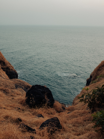 View of the vast expanse of the ocean stretches out under a hazy sky framed by the warm dry grasses of the cliffside Chiplun Maharashtra India. View of the vast expanse of the ocean stretches out under a hazy sky framed by the warm dry grasses of the cliffside Chiplun Maharashtra India.