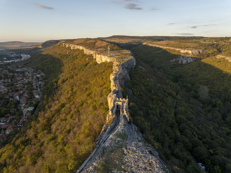Aerial view of Ovech Fortress situated on a narrow plateau with stone walls and a cross overlooking the town of Provadia during golden hour in Varna Bulgaria. Aerial view of Ovech Fortress situated on a narrow plateau with stone walls and a cross overlooking the town of Provadia during golden hour in Varna Bulgaria.
