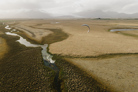 Aerial view of a kiteboarder gliding through a narrow winding stream in the vast grassy plains of the Icelandic landscape near Hofn Sveitarfelagid Hornaf Iceland.