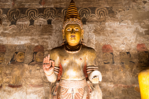 View of a golden Buddha statue with ancient mural paintings on the stone walls inside the historic cave temple in Dambulla Central Province Sri Lanka.
