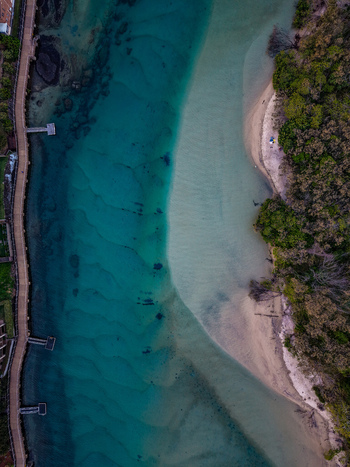 Aerial view of Cudgen Creek featuring turquoise waters sandy banks and a wooden boardwalk lined with lush vegetation in Tweed Shire Council New South Wales Australia.