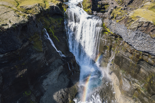 Aerial view of cascading waterfall plunges down rugged cliffs a vibrant rainbow arcing through the mist Ofaerufoss Highlands of Iceland. Aerial view of cascading waterfall plunges down rugged cliffs a vibrant rainbow arcing through the mist Ofaerufoss Highlands of Iceland.