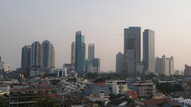 Aerial view of the modern skyline featuring high rise skyscrapers and dense residential rooftops under a hazy sky in West Jakarta Jakarta Indonesia.