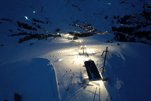 Aerial view of the illuminated ski slopes of Les Crosets at night with a chairlift station and skiers on the snow in Val d Illiez Valais Switzerland. Aerial view of the illuminated ski slopes of Les Crosets at night with a chairlift station and skiers on the snow in Val d Illiez Valais Switzerland.