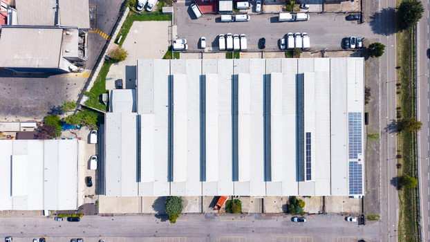 Aerial view of a self storage warehouse with a corrugated metal roof and solar panels surrounded by a parking lot with vans in Bettola Zeloforamagno Lombardia Italy.