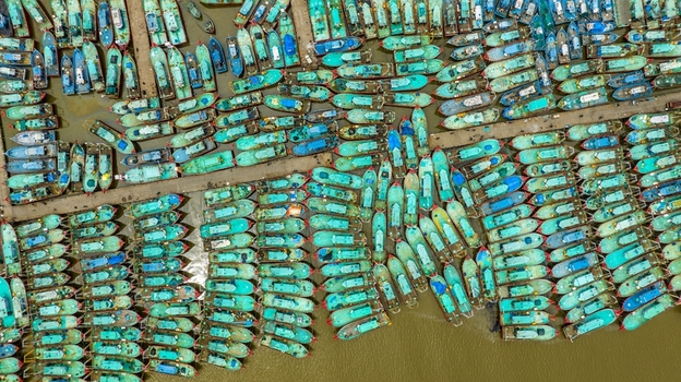Aerial view of Malpe Fishing Harbour filled with numerous turquoise fishing boats docked in rows along the concrete piers in Udupi Karnataka India. Aerial view of Malpe Fishing Harbour filled with numerous turquoise fishing boats docked in rows along the concrete piers in Udupi Karnataka India.
