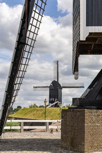 View of a traditional black wooden windmill standing on a grassy rampart with cobblestone foreground under a cloudy sky in Heusden North Brabant Netherlands.
