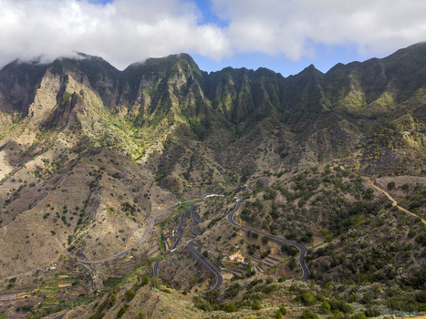 Aerial view of the rugged mountains and winding roads of La Gomera featuring lush green slopes and dramatic peaks under a cloudy sky in Santa Cruz de Tenerife Canary Islands Spain.
