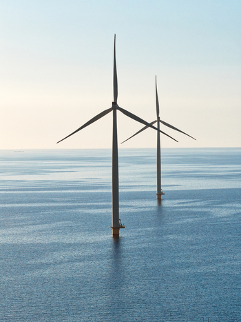 Aerial view of two offshore wind turbines standing in the calm blue sea under a clear sky Netherlands.