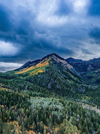 Aerial view of Alpine Loop Scenic Byway featuring vibrant autumn foliage on a mountain ridge under a dramatic cloudy sky in Utah County Utah United States. Aerial view of Alpine Loop Scenic Byway featuring vibrant autumn foliage on a mountain ridge under a dramatic cloudy sky in Utah County Utah United States.
