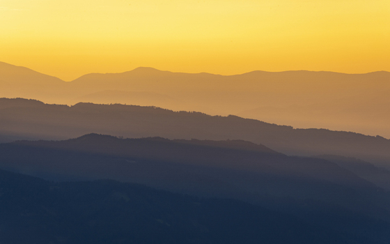 View of layered mountain ranges fading into the horizon under a warm golden sky creating a serene and majestic atmosphere Brandlalm Styria Austria. View of layered mountain ranges fading into the horizon under a warm golden sky creating a serene and majestic atmosphere Brandlalm Styria Austria.
