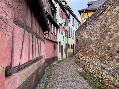 View of a narrow cobblestone street lined with traditional half timbered houses and a historic stone wall in the old town of Colmar Grand Est France.