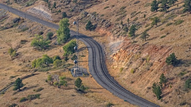 Aerial view of railway tracks winding through a hilly landscape with a communication tower and scattered trees in Golden Colorado United States.