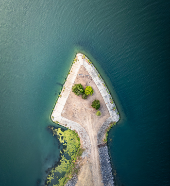Aerial view of a triangular peninsula with sparse vegetation and a dirt path extending into deep blue water in Le Pouzin Auvergne Rhone Alpes France.