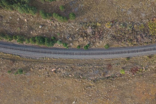 Aerial view of a railway track winding through a dry grassy landscape with scattered pine trees and rocky terrain in Golden Colorado United States.