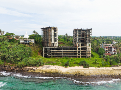 Aerial view of an unfinished concrete building structure on the coastline with a white stupa and tropical greenery in Mirissa Southern Province Sri Lanka. Aerial view of an unfinished concrete building structure on the coastline with a white stupa and tropical greenery in Mirissa Southern Province Sri Lanka.