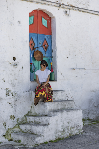View of a woman sitting on white stone steps in front of a vibrant colorful door on a traditional whitewashed building in Ostuni Apulia Italy. View of a woman sitting on white stone steps in front of a vibrant colorful door on a traditional whitewashed building in Ostuni Apulia Italy.