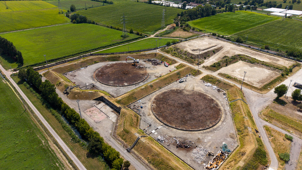 Aerial view of primary clarifier demolition at a wastewater treatment plant showing heavy machinery circular basins and surrounding fields in Tavazzano con Villavesco Lombardy Italy.