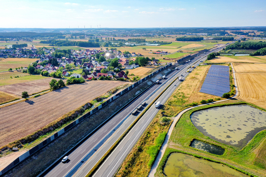 Aerial view of a highway with traffic and noise barriers passing through rural landscapes with solar panels and a small village Hochstadt Bavaria Germany. Aerial view of a highway with traffic and noise barriers passing through rural landscapes with solar panels and a small village Hochstadt Bavaria Germany.